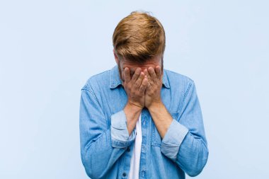 Genç, sarışın yetişkin bir adam üzgün, hayal kırıklığına uğramış, gergin ve depresif, iki eliyle yüzünü kaplayan, ağlayan