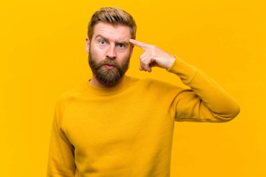 Genç sarışın adam şaşkın ve şaşkın hissediyor. Deli, deli ya da turuncu duvara karşı aklını kaçırmış olduğunu gösteriyor.