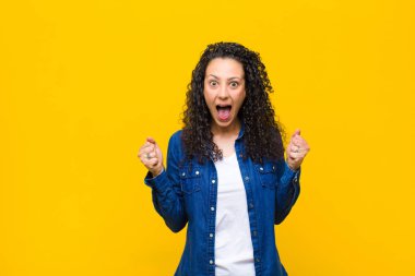 Genç, güzel bir kadın şok olmuş, heyecanlı ve mutlu, gülüyor ve başarıyı kutluyor, vay canına! turuncu duvara yaslan