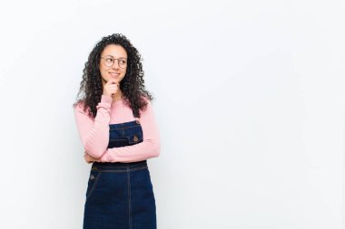 Genç, güzel bir kadın mutlu, kendinden emin bir ifadeyle gülümsüyor. Elleri çenesinde, beyaz duvara bakıyor ve merak ediyor.