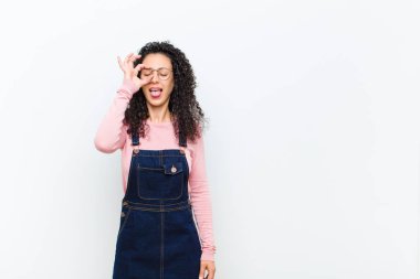 Genç ve güzel bir kadın mutlu bir şekilde gülümsüyor, şaka yapıyor ve gözetleme deliğinden bakıyor, beyaz duvara karşı sırları gözetliyor.