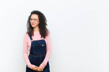 Genç, güzel bir kadın gururlu, kendinden emin, havalı, küstah ve küstah görünüyor, gülümsüyor, beyaz duvara karşı başarılı hissediyor.