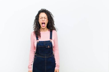 Genç ve güzel bir kadın agresif bir şekilde bağırıyor, kızgın, sinirli, öfkeli ya da sinirli görünüyor, beyaz duvara karşı hayır diye bağırıyor.