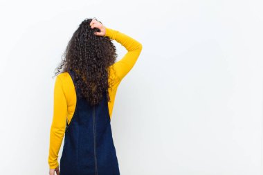 Genç, güzel bir kadın kendini cahil ve kafası karışık hissediyor, bir çözüm düşünüyor, eli kalçasında, diğeri kafasında, beyaz duvarın arkasında dikiz aynasıyla.