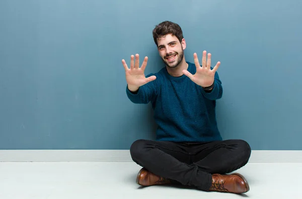 Joven Hombre Guapo Sentado Suelo Sonriendo Mirando Amigable Mostrando Número —  Fotos de Stock