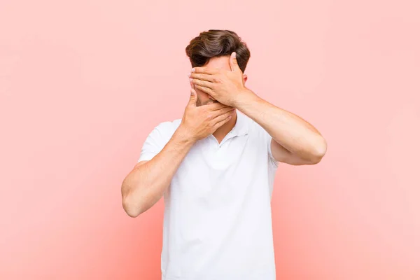 young handsome man covering face with both hands saying no to the camera! refusing pictures or forbidding photos against pink background