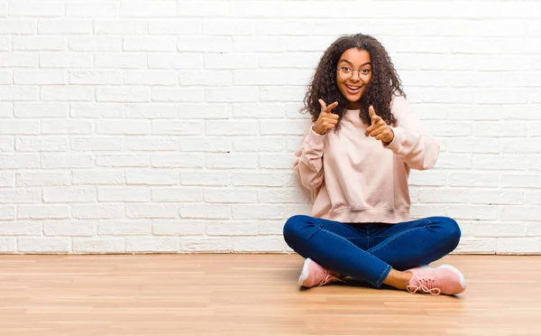 young african american black woman smiling with a positive, successful, happy attitude pointing to the camera, making gun sign with hands