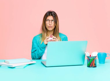 young pretty woman working with a laptop scheming and conspiring, thinking devious tricks and cheats, cunning and betraying