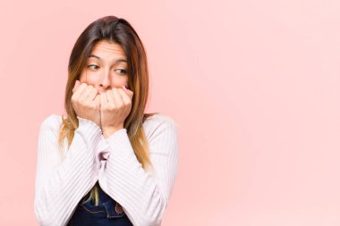 Genç, güzel bir kadın endişeli, gergin, stresli ve korkmuş görünüyor. Tırnaklarını yiyor ve beyaz arka plana karşı yanal fotokopi alanı arıyor.