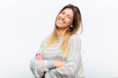 Genç ve güzel bir kadın kollarını kavuşturup mutlu bir şekilde gülüyor. Beyaz arka planda rahat, pozitif ve tatmin edici bir pozla.