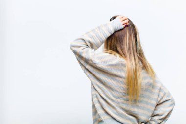 Genç, güzel bir kadın düşünüyor ya da şüphe ediyor, kafasını kaşıyor, kafası karışık ve kafası karışık hissediyor, beyaz arka planda ya da arka planda