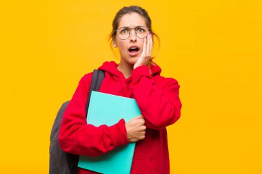 Genç ve güzel bir öğrenci şok ve inançsızlık içinde, elleri ve yanakları çaprazlanmış, sersemlemiş ve şaşırmış hissediyor.