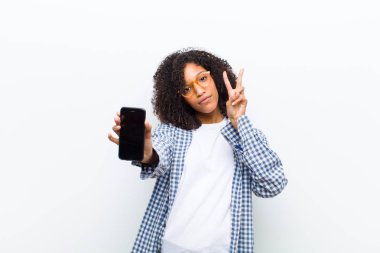 Beyaz duvarda akıllı telefonu olan genç, güzel siyah bir kadın.