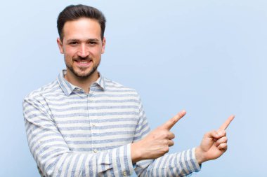 Genç yakışıklı adam mutlu bir şekilde gülümsüyor ve her iki elinde fotokopi alanında nesne gösteriyor.