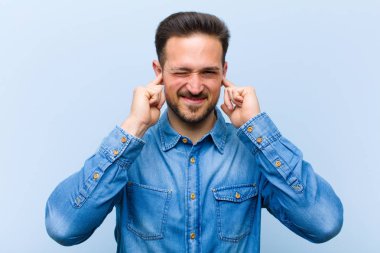 Genç yakışıklı adam sinirli, stresli ve sinirli görünüyor, iki kulağını da sağır edici bir ses, ses ya da yüksek sesle kapatıyor.