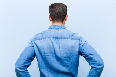Genç, yakışıklı bir adam kafası karışık ya da dolu ya da şüphe ve soru dolu, merak ediyor, elleri kalçasında, dikiz aynasından.