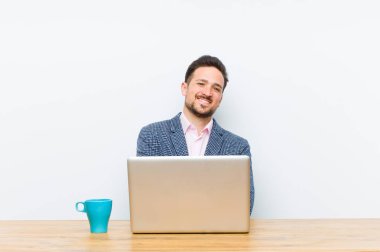 Genç yakışıklı iş adamı kollarını kavuşturup mutlu bir şekilde gülüyor, rahat, pozitif ve tatmin edici bir pozla.