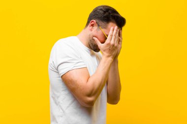 Genç ve yakışıklı bir adam, üzgün, hayal kırıklığına uğramış bakışlarıyla gözlerini kapatıyor. Ağlıyor, turuncu duvara bakıyor.