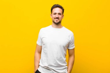 Genç ve yakışıklı bir adam neşeli bir şekilde gülümsüyor. Olumlu, mutlu, kendine güvenen ve turuncu duvara karşı gevşek bir ifadeyle.