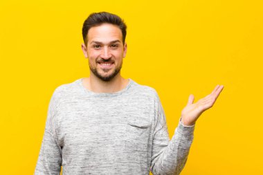 Genç yakışıklı adam kendini mutlu, şaşırmış ve neşeli hissediyor. Pozitif bir tavırla gülümsüyor. Turuncu duvara karşı bir çözüm ya da fikir buluyor.