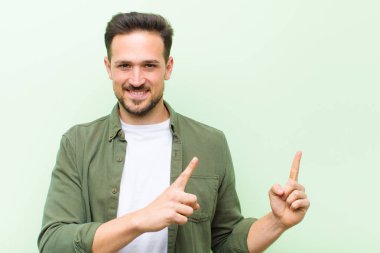 Genç yakışıklı adam mutlu bir şekilde gülümsüyor ve her iki elinde fotokopi alanında nesne gösteriyor.