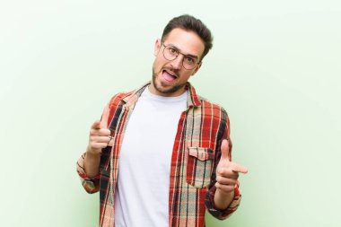 Olumlu, başarılı, mutlu bir tavırla gülümseyen genç yakışıklı adam kamerayı işaret ediyor, elleriyle silah işareti yapıyor.