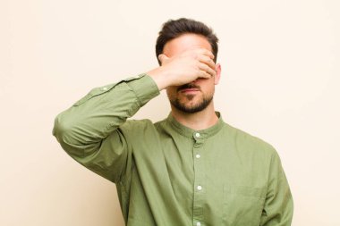 Genç yakışıklı bir adam tek eliyle gözlerini kapatıyor. Korkmuş ya da endişeli, merak ediyor ya da körü körüne bir sürpriz bekliyor.