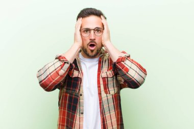 Genç ve yakışıklı bir adam hoş olmayan bir şekilde şok olmuş, korkmuş ya da endişeli görünüyor ağzı sonuna kadar açık ve iki kulağını da elleriyle kapatıyor.