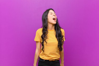 Genç, güzel Latin kadın öfkeyle bağırıyor, agresif bağırıyor, stresli ve kızgın görünüyor mor duvara karşı.