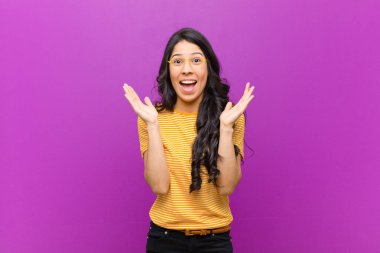 Genç ve güzel Latin kadın, mor duvara karşı beklenmedik bir sürprizden dolayı şaşkın ve heyecanlı, gülüyor, şaşkın ve mutlu hissediyor.