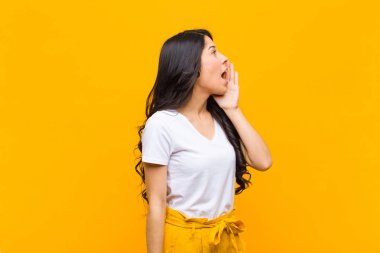 Genç ve güzel Latin kadın profil görüntüsü, mutlu ve heyecanlı görünüyor, bağırıyor ve turuncu duvara karşı fotokopi için çağırıyor.