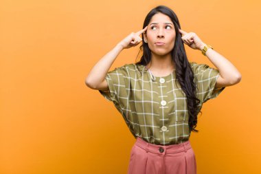 Genç ve güzel İspanyol bir kadın, kafası karışmış ya da şüpheye düşmüş, bir fikre odaklanmış, çok düşünüyor, kahverengi duvara karşı uzayı kopyalamak istiyor.