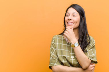 Genç, güzel, İspanyol bir kadın mutlu, kendinden emin bir ifadeyle gülümsüyor. Çenesinde elleri, kahverengi duvara bakıyor ve merak ediyor.