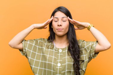 Genç, güzel, İspanyol bir kadın konsantre, düşünceli ve ilham verici görünüyor, beyin fırtınası yapıyor ve elleri alnında kahverengi duvarda hayal kuruyor.