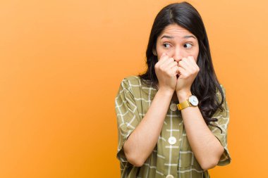 Genç, güzel İspanyol kadın endişeli, stresli ve korkmuş görünüyor. Tırnaklarını yiyor ve kahverengi duvara karşı yanal fotokopi çekmeye çalışıyor.