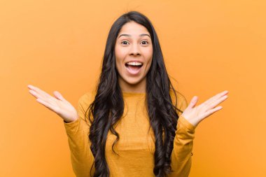 Genç, güzel İspanyol kadın mutlu ve heyecanlı görünüyor. Beklenmedik bir sürprizle şoke olmuş. İki eli de kahverengi duvarın yanında.