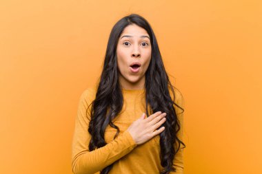 Genç ve güzel İspanyol kadın şok olmuş ve şaşırmış hissediyor, gülümsüyor, el ele tutuşuyor, o kişi olmaktan mutlu ya da kahverengi duvara karşı minnettarlık gösteriyor.