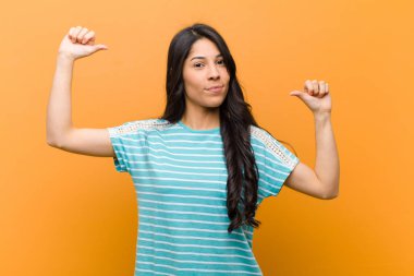 Genç, güzel İspanyol bir kadın gururlu, kibirli ve kendinden emin, tatmin olmuş ve başarılı görünüyor, kahverengi duvara karşı kendini işaret ediyor.