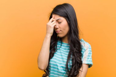 Genç ve güzel İspanyol kadın stresli, mutsuz ve hayal kırıklığına uğramış, alnına dokunmuş ve kahverengi duvara karşı şiddetli baş ağrısı çeken.