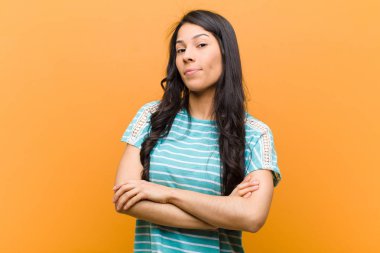 Genç, güzel, İspanyol bir kadın hayal kırıklığına uğramış, hayal kırıklığına uğramış, ciddi görünüyor, kızgın ve kahverengi duvara karşı çapraz kollara sahip