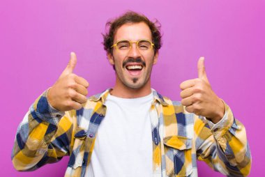 Genç yakışıklı adam gülümsüyor. Mutlu, pozitif, kendinden emin ve başarılı. İki başparmağı da mor duvarda.