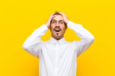 Genç yakışıklı adam el ele tutuşuyor, ağzı açık, son derece şanslı, şaşkın, heyecanlı ve turuncu duvara karşı mutlu hissediyor.