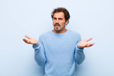 Genç ve yakışıklı bir adam bilgisiz ve şaşkın hissediyor, hangi seçeneği seçeceğinden emin değil, düz duvara karşı izole edilmiş merak ediyor.