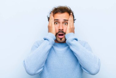 Genç ve yakışıklı bir adam mutsuz, korkmuş ya da endişeli görünüyor, ağzı sonuna kadar açık ve iki kulağı da kapalı ve elleri düz duvara yaslanmış.