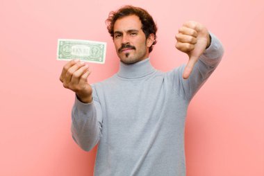 Pembe düz duvarda dolar banknotları olan genç yakışıklı bir adam.