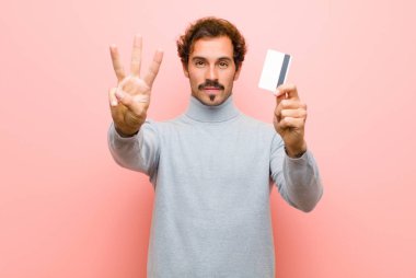 Pembe düz duvara karşı kredi kartı olan genç ve yakışıklı bir adam.