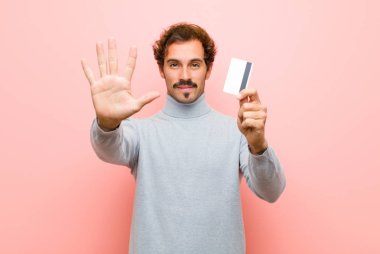 Pembe düz duvara karşı kredi kartı olan genç ve yakışıklı bir adam.