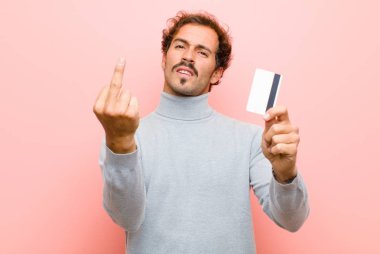Pembe düz duvara karşı kredi kartı olan genç ve yakışıklı bir adam.