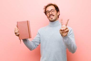 Pembe düz duvara karşı not defteri olan genç yakışıklı adam.