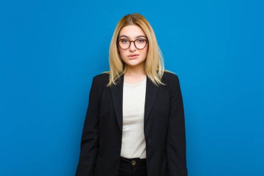 Şaşkın ve kafası karışmış genç sarışın kadın gergin bir hareketle dudağını ısırıyor, düz duvara karşı sorunun cevabını bilmiyor.